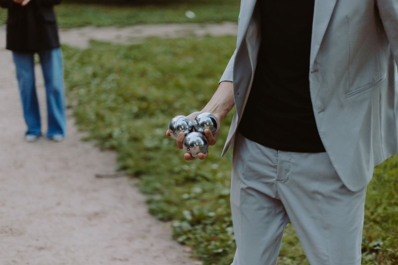 who-we-are A person holding stainless steel boules on a park pathway, ready to play.