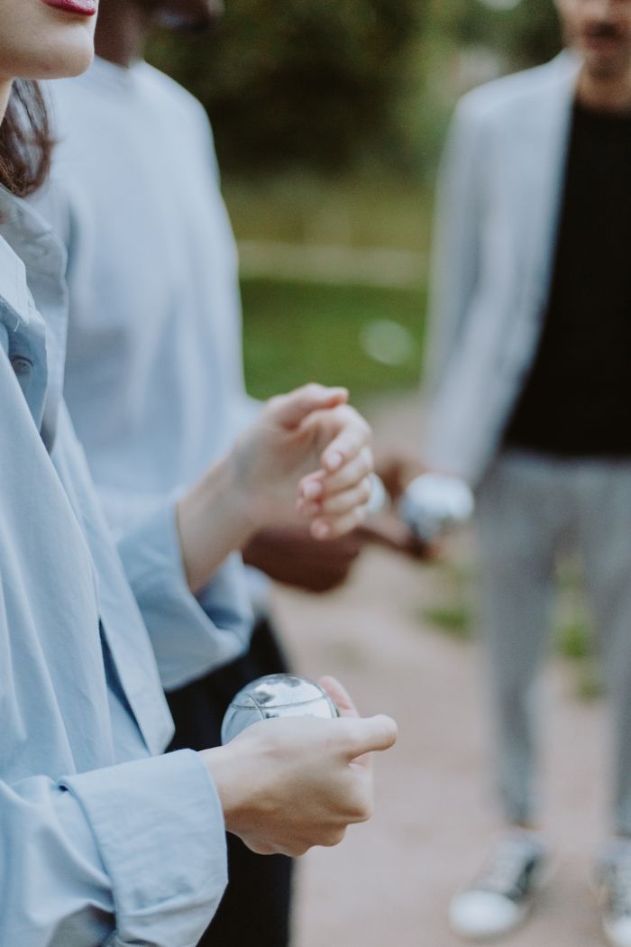 our-story Close-up of adults enjoying leisure time outdoors with metallic balls, focusing on hands and activity.
